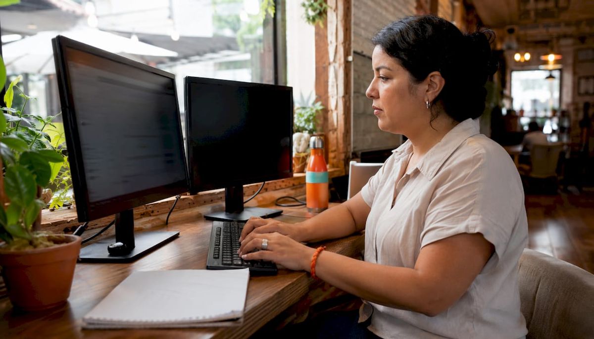 Software specialist typing at dual monitors in home office
